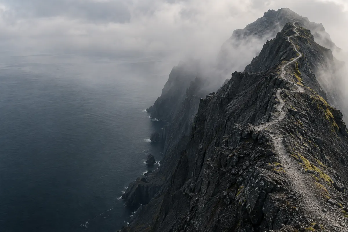 A narrow path leading through dark, mist-covered mountains